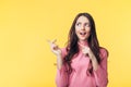 Beautiful surprised woman pointing finger at copy space looking away isolated on yellow background