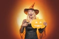 Beautiful surprised woman in witches hat and costume - showing products. Halloween Woman portrait. Beauty Woman posing