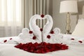 Beautiful swans made of towels and red rose petals on bed in room Royalty Free Stock Photo