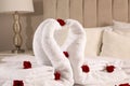 Beautiful swans made of towels with red roses on bed in room, closeup Royalty Free Stock Photo