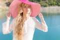 Beautiful sweet gentle girl in white dress in light big pink hat on the shore of the blue sea at sunset summer evening sun Royalty Free Stock Photo