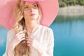 Beautiful sweet gentle girl in white dress in light big pink hat on the shore of the blue sea at sunset summer evening sun