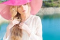 Beautiful sweet gentle girl in white dress in light big pink hat on the shore of the blue sea at sunset summer evening sun Royalty Free Stock Photo