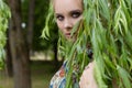 Beautiful sweet tender girl blonde with blue eyes stands near a tree with long branches with a sprig of flowers in her hands Royalty Free Stock Photo