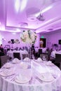 Beautiful table setting with crockery and white flower arrangement in a vase on a high stem for a party, wedding reception or