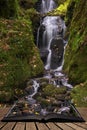 Beautiful tall waterfall flowing over lush green landscape foliage in early Autumn coming out of pages of open story book