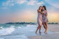 A girl in a dress hugs her mom in a dress while walking along the beach near the sea with waves Royalty Free Stock Photo