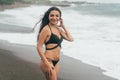 Beautiful tanned girl in black swimsuit resting on black sand beach. Attractive brunette woman has rest alone on ocean Royalty Free Stock Photo