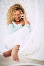 Beautiful tanned lady sit down on a white coach outdor in uxury place do a phone call with friends - concept of hotel summer Royalty Free Stock Photo