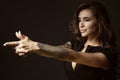 Beautiful tattooed woman with luxuriant shining wavy hair and perfect make up pretending to aim something with shooting gesture Royalty Free Stock Photo