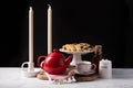 Beautiful tea setting in black background with a Red tea pot, honey, sugar, candle and some biscuits Royalty Free Stock Photo