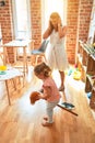 Beautiful teacher and blond student toddler girl ridding horse toy with stick at kindergarten