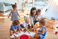 Beautiful teacher and group of toddlers sitting on the floor drawing using paper and pencil around lots of toys at kindergarten