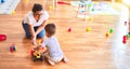 Beautiful teacher and toddler boy playing with tractor and cars at kindergarten