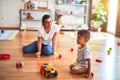 Beautiful teacher and toddler boy playing with tractor and cars at kindergarten