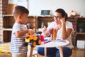 Beautiful teacher and toddler boy playing with tractor and cars at kindergarten