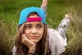 Beautiful teen girl with big eyes in a baseball cap lies on the grass and looks away Royalty Free Stock Photo