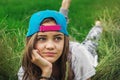 Beautiful teen girl with big eyes in a baseball cap lies on the grass and looks away Royalty Free Stock Photo