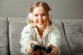 Beautiful teen girl blonde playing video console game using game controller joystick gamepad sitting on couch sofa. Happy young Royalty Free Stock Photo