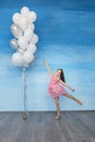 A beautiful teen girl with brown hair in a pink dress is standing against a blue sky background and holding a lot of balloons. Royalty Free Stock Photo