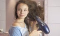 Beautiful teen girl dries hair a hairdryer in bathroom Royalty Free Stock Photo