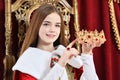 Beautiful teen girl holding crown sitting in vintage armchair