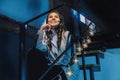 Beautiful teen girl in a light jacket sitting on a metal ladder in a dark room near the burning lamps and smiling