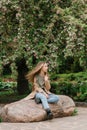 Beautiful teen girl with long blonde hair sits on a rock in the park Royalty Free Stock Photo