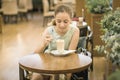 Beautiful teen girl stirring cream in coffee in tall glass at cafe