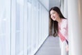 Beautiful teenage Asian girl wears a white with pink shirt and smiles cheerfully look outside while she stands near the glassed