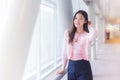 Beautiful teenage Asian girl wears a white with pink shirt and smiles cheerfully while she stands near the glassed window on a