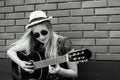 Beautiful teenage blonde long haired girl playing acoustic guitar outdoor. Vertical black and white color image. Royalty Free Stock Photo