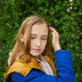 Beautiful teenage blonde schoolgirl in a blue and yellow coat in park in autumn Royalty Free Stock Photo