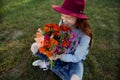 a beautiful teenage girl in a big red hat is sitting with a bouquet of flowers on the green grass Royalty Free Stock Photo