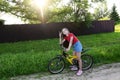 beautiful teenage girl in denim shorts and T-shirt is learning to ride bicycle through streets of summer village on sunny day.