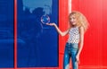 Beautiful teenage girl inflates soap bubbles in front of the red-blue wall Royalty Free Stock Photo
