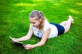 Beautiful teenage girl lies on green grass and reads book in park on summer sunny day Royalty Free Stock Photo