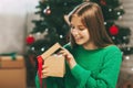 Beautiful teenage girl opens a gift made of kraft paper tied with a red ribbon, new year mood. Holiday concept of Christmas and Royalty Free Stock Photo