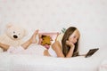 Beautiful teenage girl in pajamas is lying on her bed and watching a video movie on her tablet Royalty Free Stock Photo