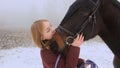 A beautiful teenage girl playfully kisses a brown horse in a foggy field. Royalty Free Stock Photo