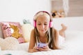 Beautiful teenage girl is relaxing in bed using a touchscreen smartphone, listening to music Royalty Free Stock Photo