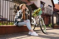 Beautiful teenage girl sitting near bicycle with bouquet of yellow tulips on city street Royalty Free Stock Photo