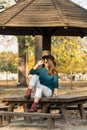 Beautiful teenage girl sitting on the park bench with black hat blue sweater and ripped jeans with blurred autumn leaves in the ba Royalty Free Stock Photo