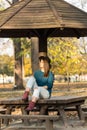 Beautiful teenage girl sitting on the park bench with black hat blue sweater and ripped jeans with blurred autumn leaves in the ba Royalty Free Stock Photo