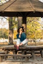 Beautiful teenage girl sitting on the park bench with black hat blue sweater and ripped jeans with blurred autumn leaves in the ba Royalty Free Stock Photo