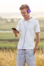 Beautiful teenager boy in headphones listening to music on nature, young blond man relaxing in summer field, concept youth Royalty Free Stock Photo