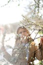 Beautiful teenager girl looking through the blooming apricot tree branch at spring, blurred image with sunlight backlighting haze Royalty Free Stock Photo