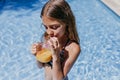 Beautiful teenager girl at the pool drinking healthy orange juice and having fun outdoors. Summertime and lifestyle concept Royalty Free Stock Photo