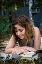 Beautiful teenager girl reading a book lying on blanket on green grass at the forest Royalty Free Stock Photo