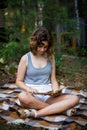 Beautiful teenager girl reading a book lying on blanket on green grass at the forest Royalty Free Stock Photo